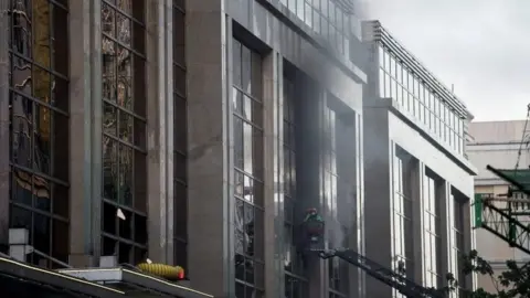 AFP/Getty Images Firemen break a glass window of the Resorts World Hotel following an assault in Manila on 2 June 2017.