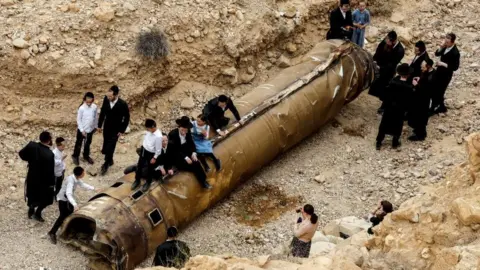 Reuters Israelis hang around the apparent remains of a ballistic missile in southern Israel, 26 April