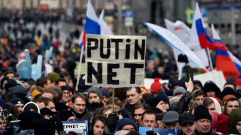 Getty Images A protester holds a placard reading "Putin - No!" during an opposition rally in central Moscow, on 10 March