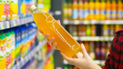 Getty Images Woman holding a bottle of orange squash