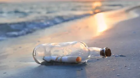 Getty Images A bottle on a beach, with a note inside