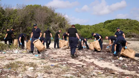 Royal Navy a group of people collect plastic on a beach