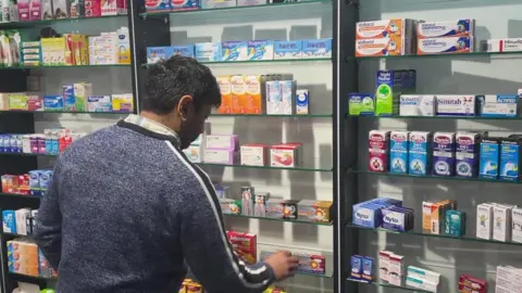 Empics Faisel Baig behind the counter at his pharmacy