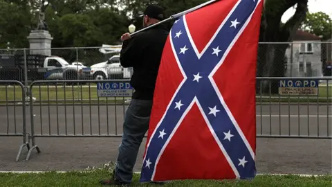 Getty Images A man holding a Confederate flag across the street from the Jefferson Davis monument in New Orleans, Louisiana