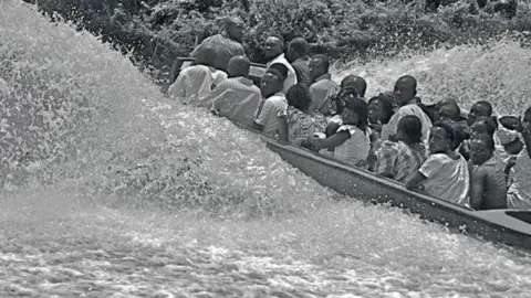 Sunmi Smart-Cole A photo by Sunmi Smart-Cole entitled: "Stormy Times In The Niger Delta" - 2006, showing people on a speedboat in the Niger Delta, Nigeria