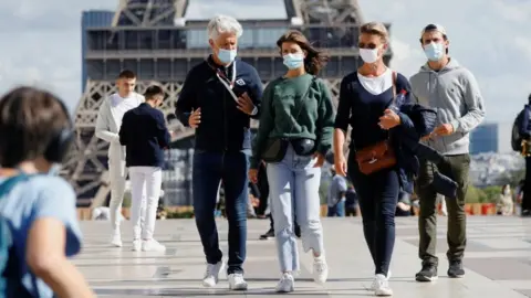 Reuters People wearing protective masks walk at the Trocadero square near the Eiffel Tower in Paris