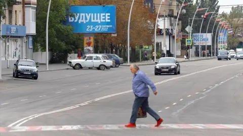 Reuters A man crosses a street as a banner informing about the referendum - and reading "Future. 23-27 September 2022" - is seen in the background - Melitopol, 26 September 2022