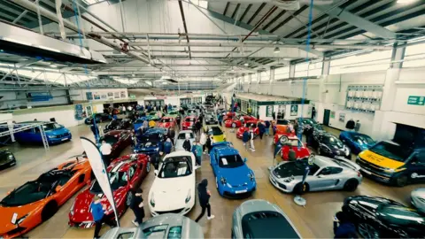 Tony Clark An indoor hanger full of cars with people around the edge studying them