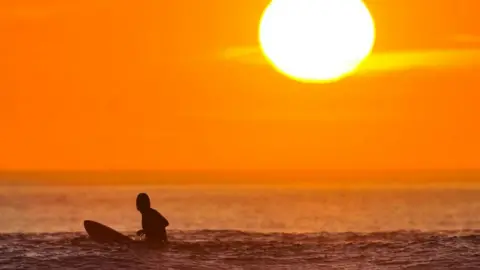 Ben Birchall/PA Wire A surfer in the sunset