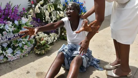 Getty Images A woman, helped by a relative, cries next to wreaths of flowers in front of the Etoile du Sud hotel on March 20, 2016 in Grand Bassam, during a tribute to the victims of a djihadist attack that killed 19 people on March 13