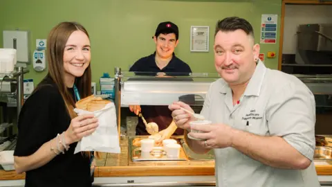 RJAH Pictured is Alex Mendez, Catering Assistant; serving Olivia Evans, Improvement Lead; and Karl Mcguire, Healthcare Assistant; free toast and porridge at breakfast.