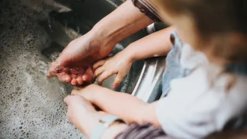 The hands of a parent and child are seen in a sink