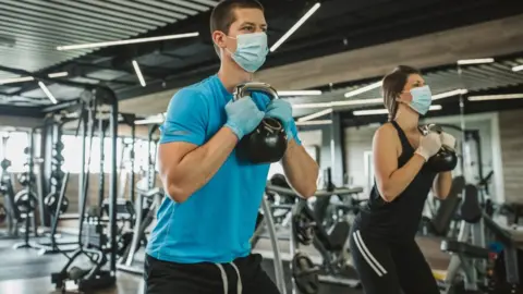 Getty Images Man and woman wearing masks working out at a gym