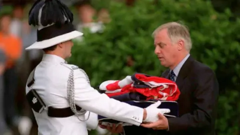Getty Images Chris Patten, as the outgoing Governor of Hong Kong, seen here receiving the Union Jack flag and Hong Kong Colonial flag as part of the handover ceremony in 1997