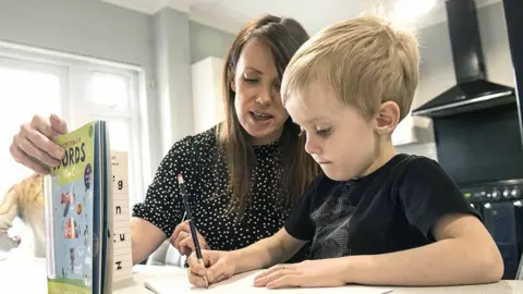 PA Media Little boy working on schoolbook with mother at home