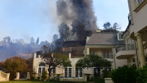 AFP A huge plume of black smoke rises from a burning home on a hilltop beside one still standing in Bel Air, east of the 405 freeway on December 6, 2017 in Los Angeles, California