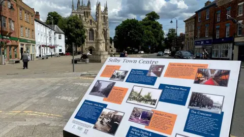 Selby Abbey, Market Cross and an information sign in the foreground