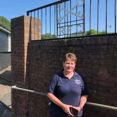 Cross Keys Rugby Club secretary Angie Prangell standing beneath a club sign