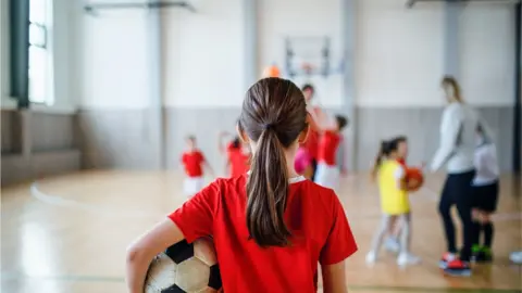 Getty Images Girl holding a ball in a school sports lesson