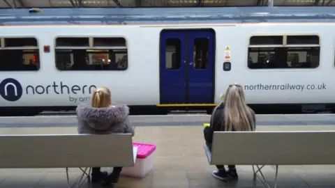 BBC women sit on platform looking at northern railway train