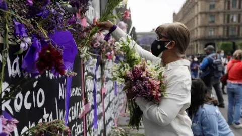 Reuters A woman places flowers beside the names of victims of femicide in Mexico on fences placed outside the National Palace ahead of a Women"s Day protest in Mexico City, Mexico March 7, 2021