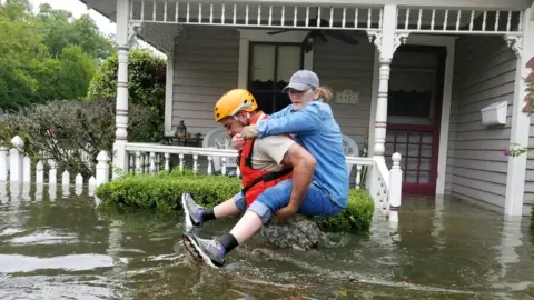 Reuters A soldier, waist-deep in water, carried a woman on his back past the front of a house porch