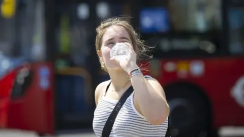 Getty Images Woman drinks from water bottle during hot weather