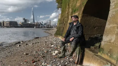 Matthew Williams-Ellis/Thames & Hudson Malcom Russell sitting on an arch on the foreshore of the Thames