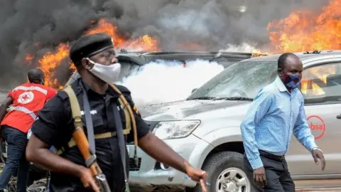 People extinguish fire on cars caused by a bomb explosion near Parliament building in Kampala, Uganda, on November 16, 2021.