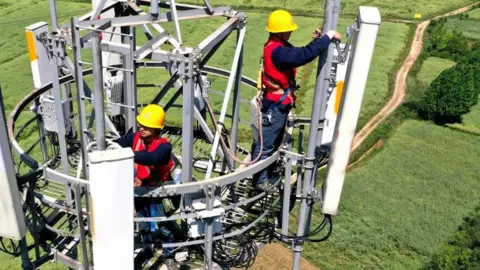 Getty Images Workers installing a 5G phone mast