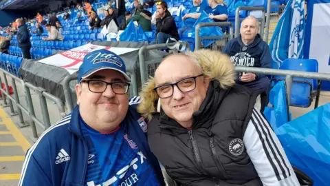 Steve Kirby Steve Kirby and Gary Battle standing in the Sir Bobby Robson stand ahead of an Ipswich Town game. Both wearing Ipswich Town clothing