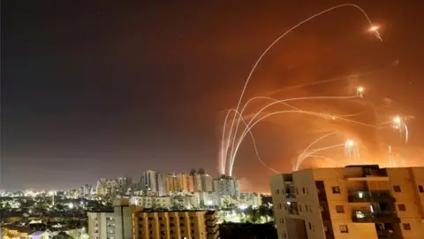 Reuters Streaks of light are seen as Israel's Iron Dome anti-missile system intercept rockets launched from the Gaza Strip, as seen from Ashkelon, Israel (12 May 2021)