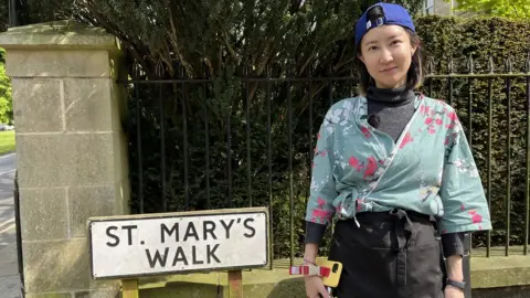 BBC / Naj Modak Lady stood in front of old street sign