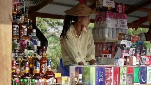 BBC/ Lulu Luo A Burmese woman selling cigarette and alcohol at a Thai Myanmar border market
