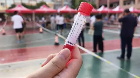 VCG/VCG via Getty Images A local resident holds a test tube used to collect samples for Covid testing in Henan province