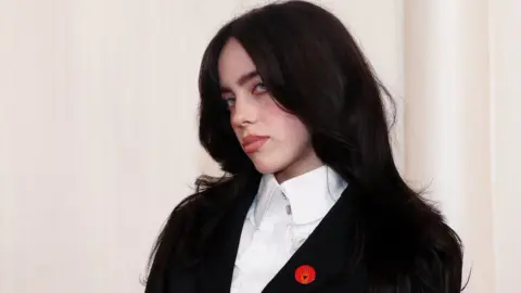 Reuters Billie Eilish at the 86th Academy Awards, wearing a black suit jacket with a white shirt and a red pin