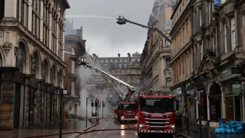 PA Media Firefighters damp down the remains of the fire on Union Corner. Two fire engines and several high-rise appliances are on the street. 