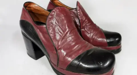 John Rolfe Auctions A pair of red and black leather heeled platform shoes. They are mostly red with a black toe, black heel and black piping around the tongue.