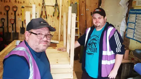 Dorset Community Foundation Two men in purple hi vis jackets doing wood work