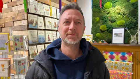 Karl Shaw, with grey hair and beard wearing a navy blue hoodie and black coat