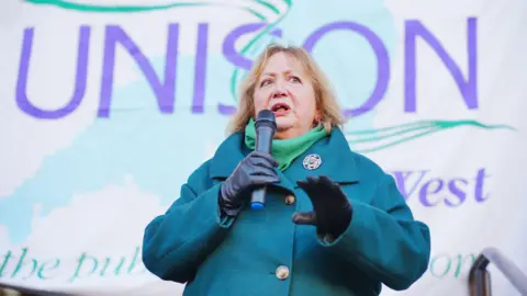 PA Media Christina McAnea speaks into a microphone at a rally in November. She is standing in front of a Unison sign.