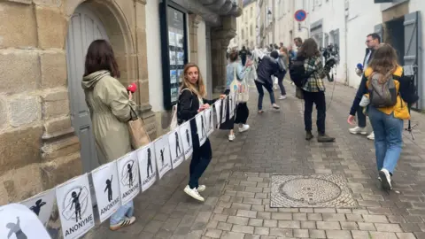 A long banner representing the many victims of Le Scouarnec being unfurled in the streets of Vannes