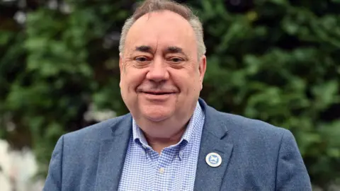 Getty Images Smiling Alex Salmond wearing an Alba badge pinned to his blue suit jacket