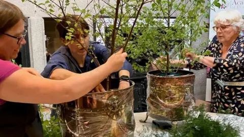 British Academy of Floral Art Three people arrange plants in pots.
