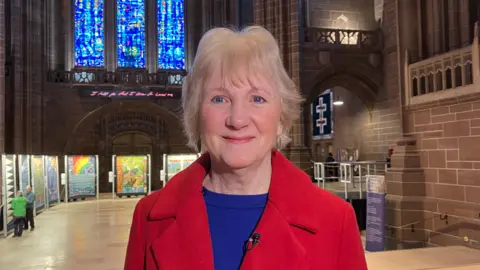 Jacqui Parkinson, wearing a red jacket, standing in her exhibition space in the vast gothic-style Liverpool Cathedral