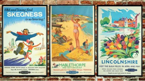 North East Lincolnshire Council Three posters side by side: the jolly fisherman to the left, one in the middle advertises Mablethorpe and Sutton on Sea, and features a slim lady in a striped bikini on the sand while children play nearby.  The third one says "Lincolnshire: visit the bulb fields in April and May".