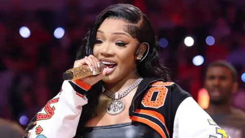 GloRilla in a colourful jacket singing into a gold-studded microphone at the WNBA All-Star Game