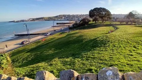 Dorset Coast Forum Stone wall looking towards large green area and sea and beach to the left.