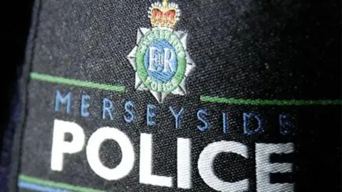 A close-up of an embroidered Merseyside Police badge on black material. 