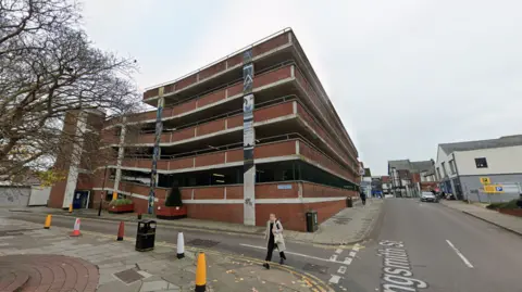 A Google street view shot of the longsmith street carpark. It is a five-floor brick car park on a side road off a main high street with some faded artwork on the side.